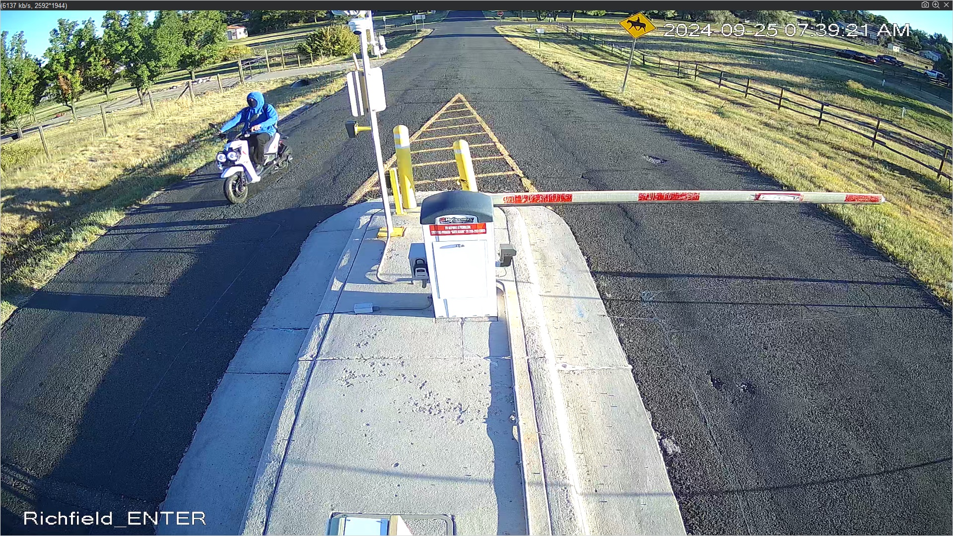 Person with blue hoodie on white scooter approaching gate on opposite side