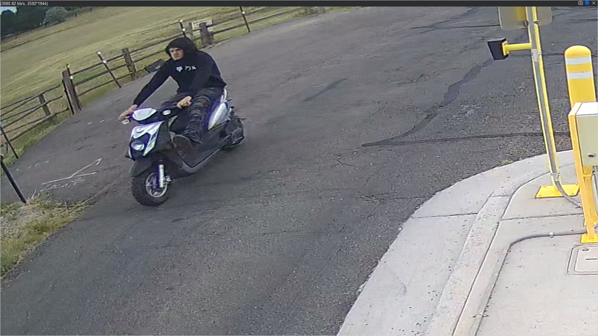 Man driving blue and silver scooter down Richfield wearing black hoodie and blue jeans. Foot propped up to kick gate arm.